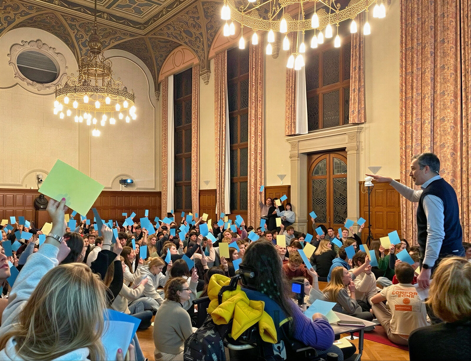 Imre Végh on stage in a grand hall, the audience holding up coloured cards