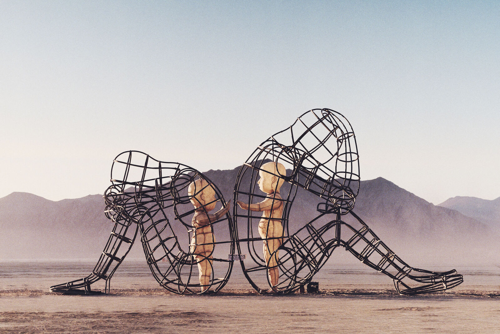 Love sculpture by Alexander Milov at Burning Man, adults turned away, inner children reaching toward each other
